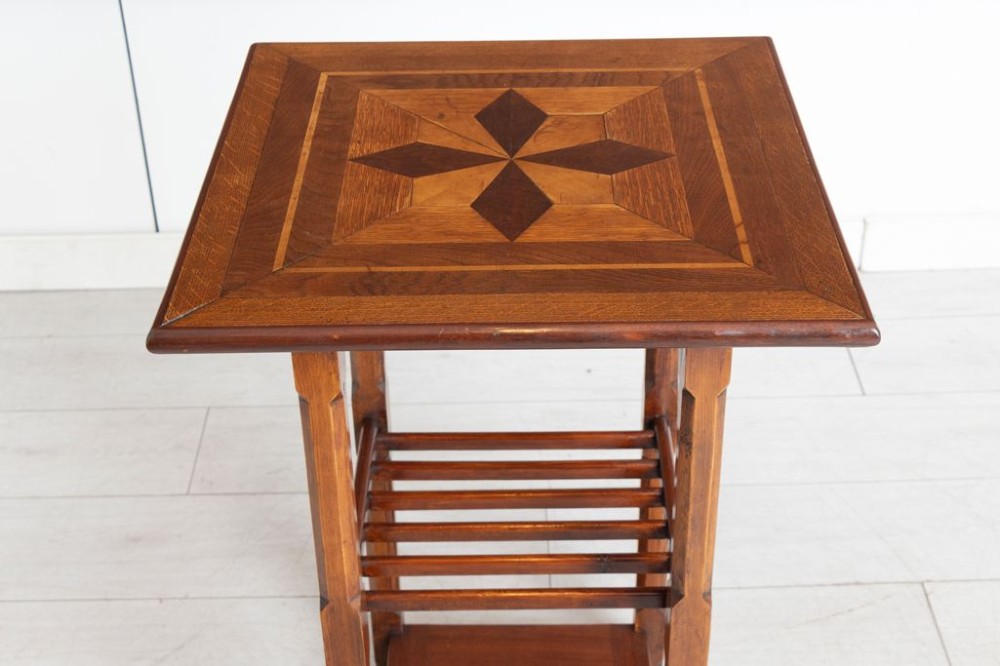 An Arts and Crafts square wooden side table featuring geometric inlaid timber patterns on the top, chamfered legs, a slatted middle shelf, and a solid lower shelf. View II