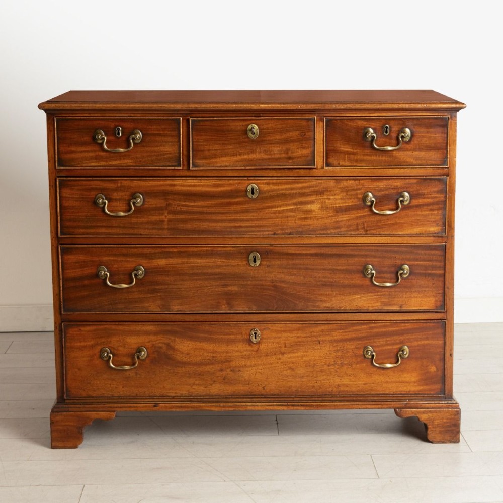 A George III mahogany chest of drawers featuring three small top drawers above three full-width drawers with brass handles and bracket feet.