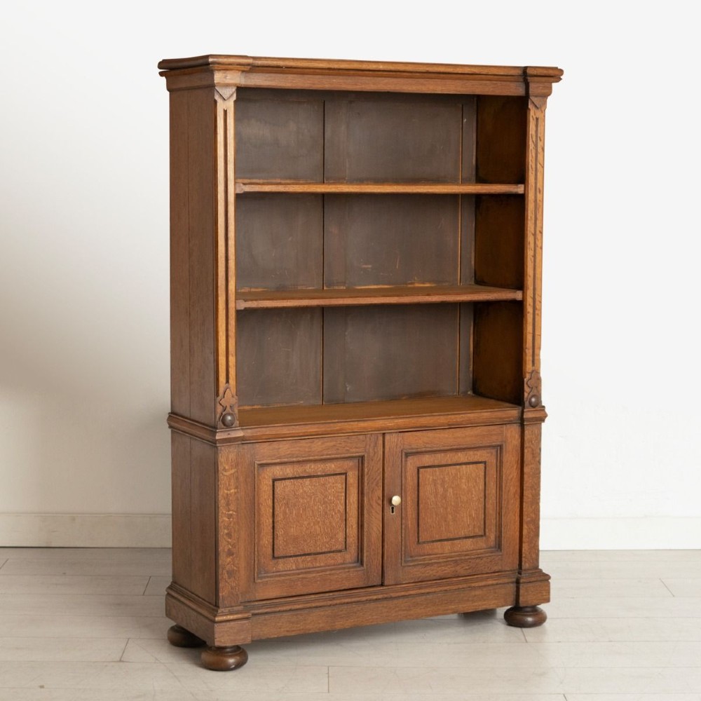 A late 19th-century oak open bookcase featuring two upper shelves above a double-door panelled cupboard base on turned bun feet.