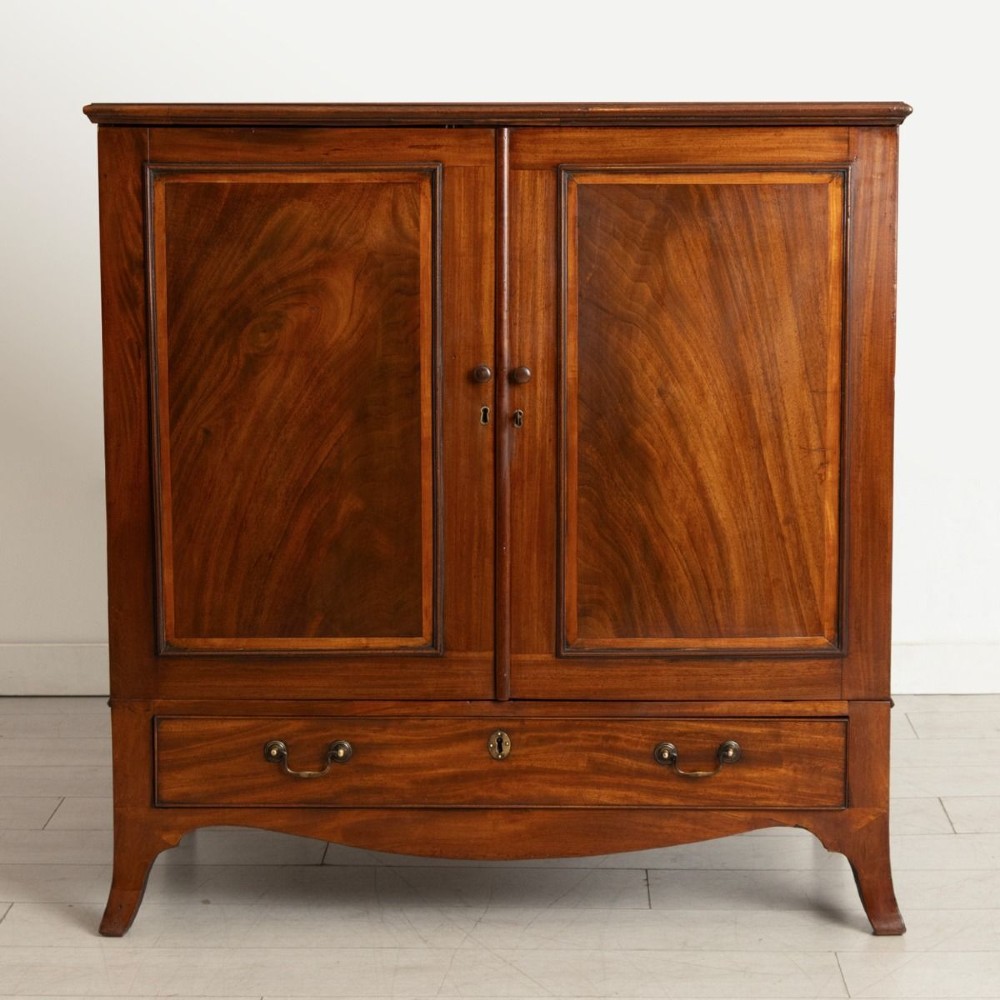 A small Georgian mahogany linen press featuring twin panelled doors with flame grain veneers above a single drawer on a shaped apron base. View II
