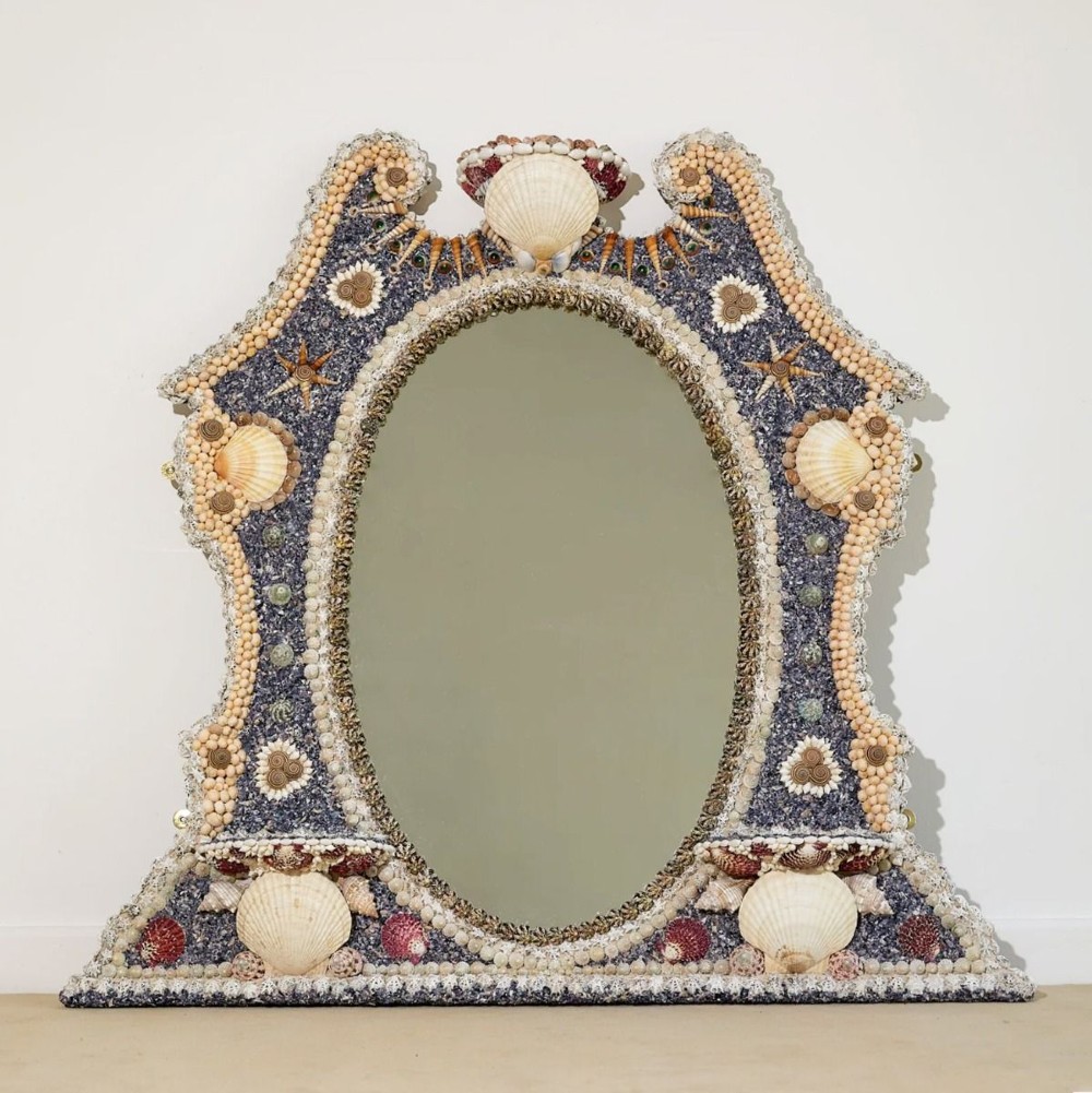 An architectural Georgian wall mirror frame encrusted with natural cream shells and dark blue mineral accents surrounding a central oval glass plate.