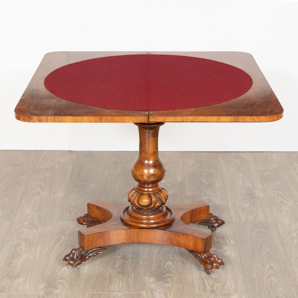 A mid-19th century Victorian burr walnut games table featuring a fold-over rectangular top resting on a turned bulbous pedestal column and a quadripartite base with carved feet on castors. View III