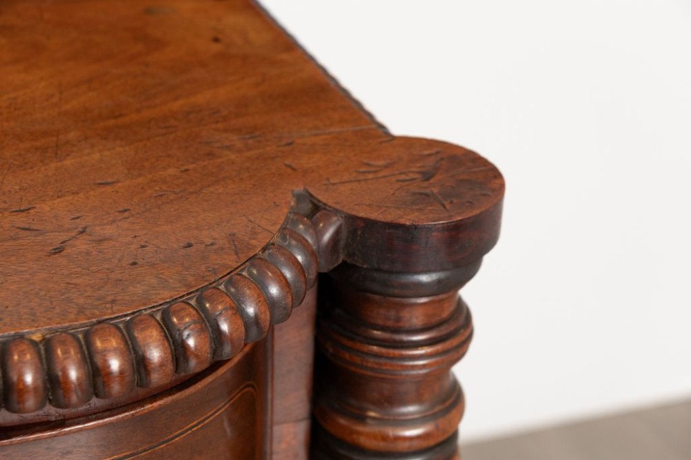 An antique William IV flame mahogany chest of drawers featuring turned spiral columns, multiple small top drawers around a central hat drawer, and wooden turned knobs. View III