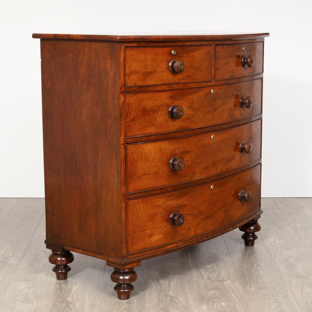 A nineteenth-century Victorian mahogany chest of drawers featuring a bow-front silhouette, four graduated drawers with turned wood knobs, brass keyholes, and turned feet. View II