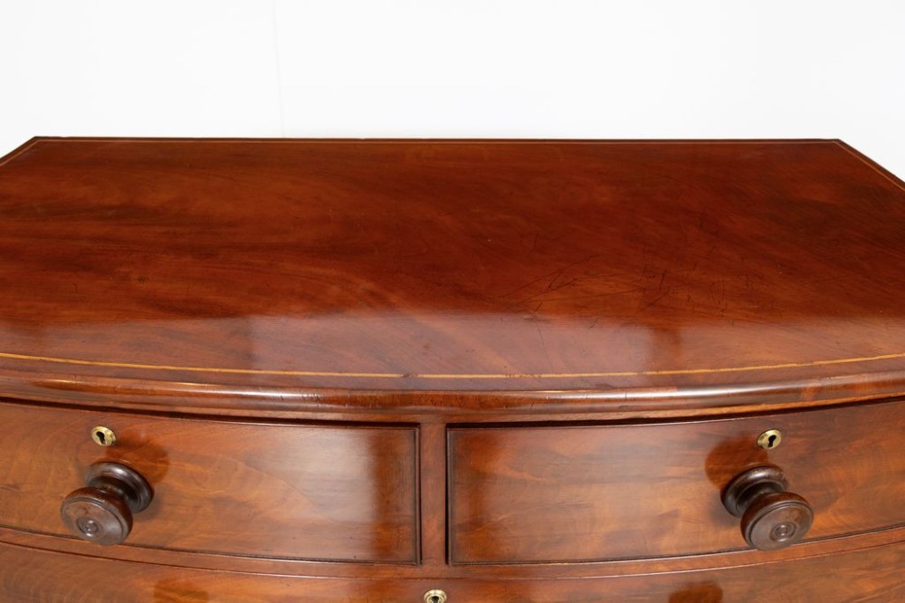 A nineteenth-century Victorian mahogany chest of drawers featuring a bow-front silhouette, four graduated drawers with turned wood knobs, brass keyholes, and turned feet. View IV