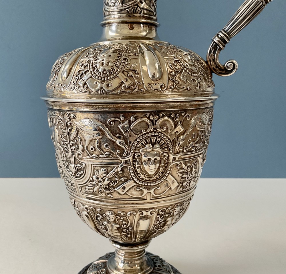 A detailed solid silver Cellini pattern ewer decorated with chased relief masks, scroll motifs, and a sculpted handle atop a pedestal base. View VIII