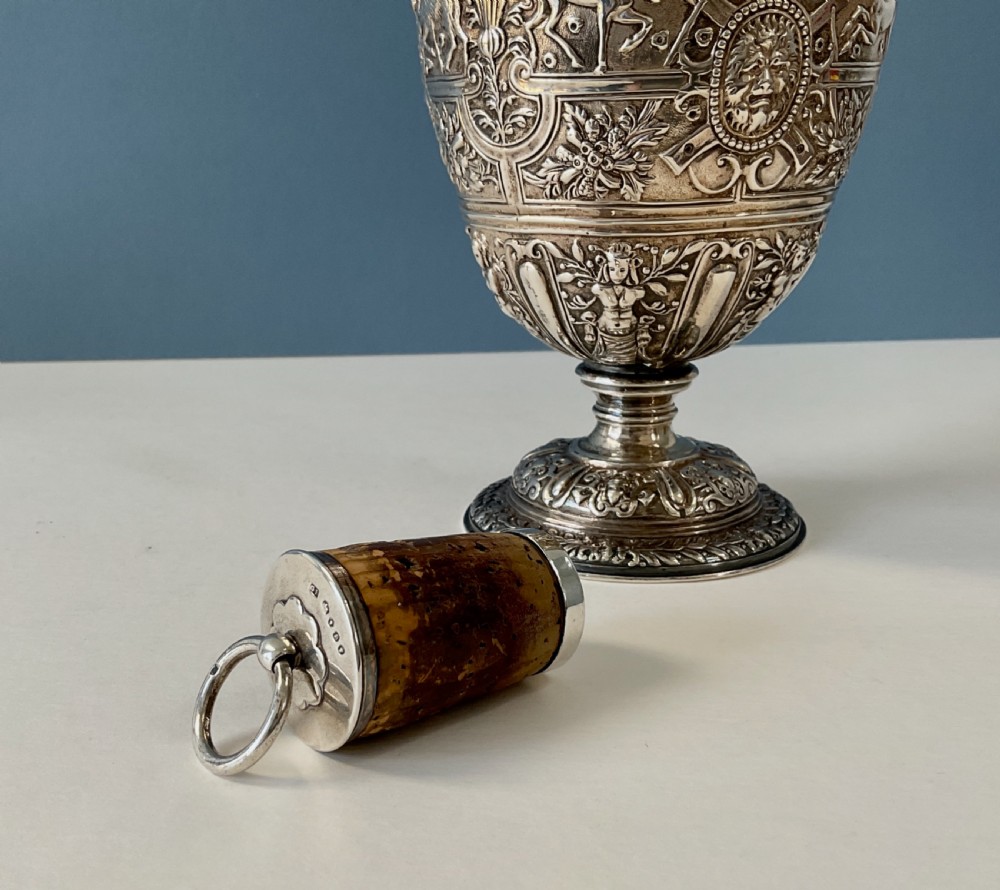 A detailed solid silver Cellini pattern ewer decorated with chased relief masks, scroll motifs, and a sculpted handle atop a pedestal base. View X