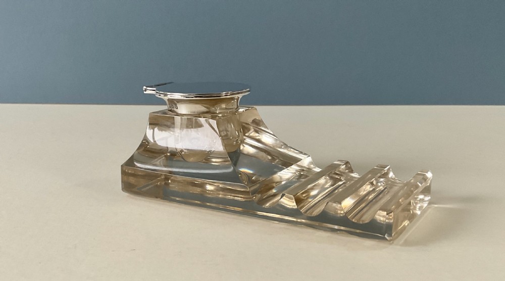 An antique clear glass inkstand featuring a built-in pen tray and an integrated glass inkwell topped with a silver hinged lid.