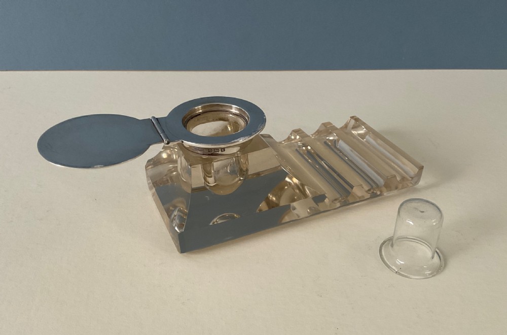 An antique clear glass inkstand featuring a built-in pen tray and an integrated glass inkwell topped with a silver hinged lid. View III