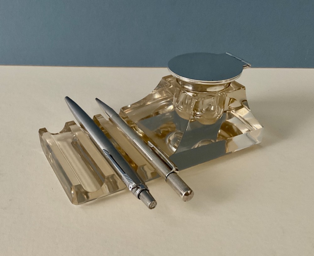 An antique clear glass inkstand featuring a built-in pen tray and an integrated glass inkwell topped with a silver hinged lid. View VI