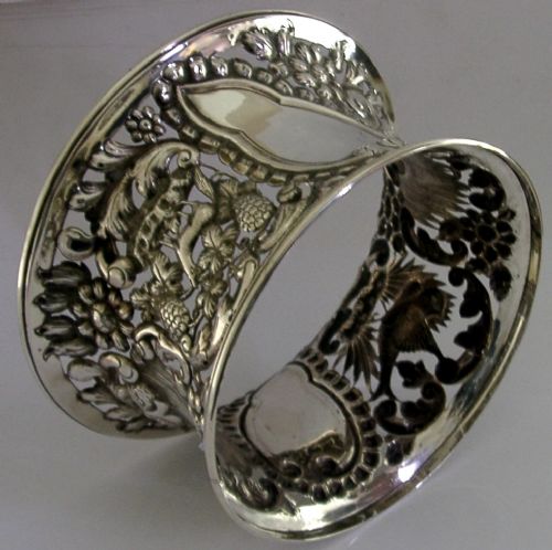 An hourglass-shaped sterling silver dish ring featuring intricately pierced fretwork with floral motifs, scrolls, and marine life details. View IX