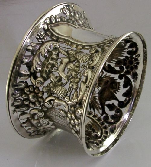 An hourglass-shaped sterling silver dish ring featuring intricately pierced fretwork with floral motifs, scrolls, and marine life details. View X