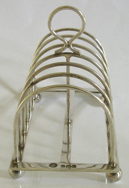 A sterling silver six-slice toast rack featuring seven arched wire divisions, a central loop handle, and four ball feet resting on a rectangular base. View IV