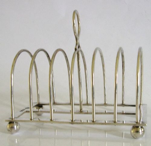 A sterling silver six-slice toast rack featuring seven arched wire divisions, a central loop handle, and four ball feet resting on a rectangular base. View VI