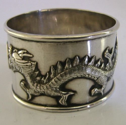 A cylindrical silver napkin ring featuring a relief-carved Chinese dragon motif against a polished surface. View II