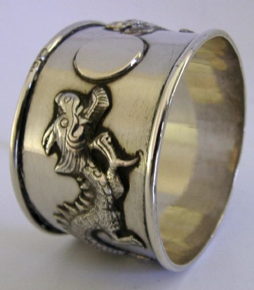 A cylindrical silver napkin ring featuring a relief-carved Chinese dragon motif against a polished surface. View III