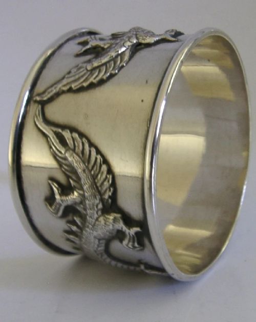 A cylindrical silver napkin ring featuring a relief-carved Chinese dragon motif against a polished surface. View IV