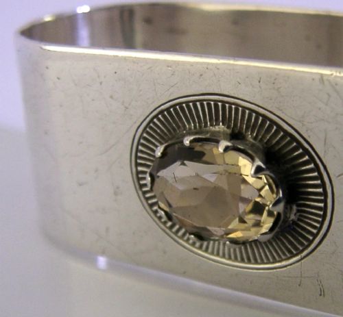 A flat sterling silver napkin ring featuring a central oval faceted citrine gemstone framed by a radiant engraved sunburst motif. View II