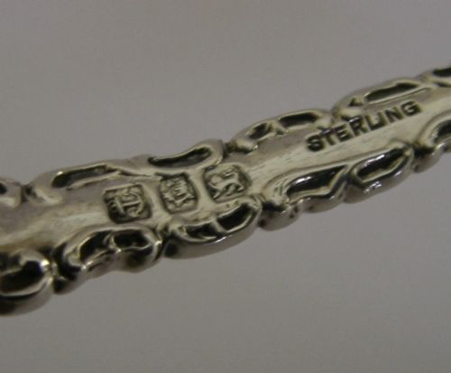 An antique sterling silver serving spoon featuring a scalloped shell-shaped bowl and an ornate scrollwork handle. View V