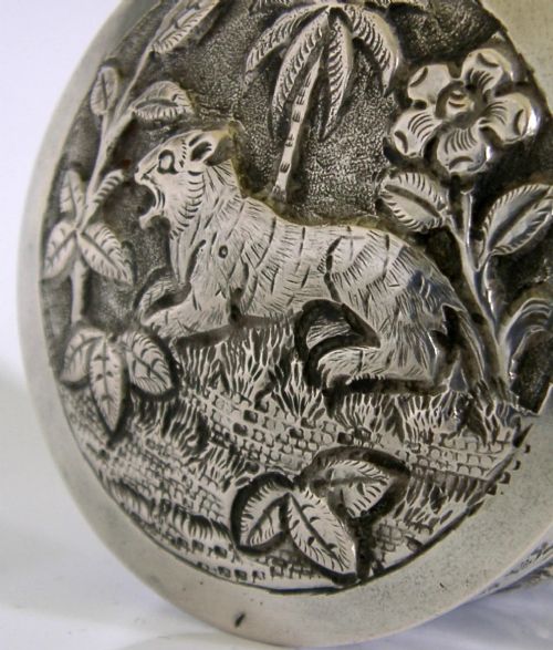 A cylindrical antique Indian solid silver caddy box with a fitted lid, decorated with embossed repousse relief depicting trees, foliage, and village huts. View II