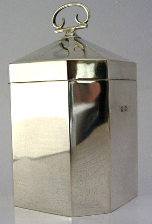An octagonal sterling silver tea caddy featuring a faceted domed lid, scroll finial, and British hallmarks stamped near the rim. View II