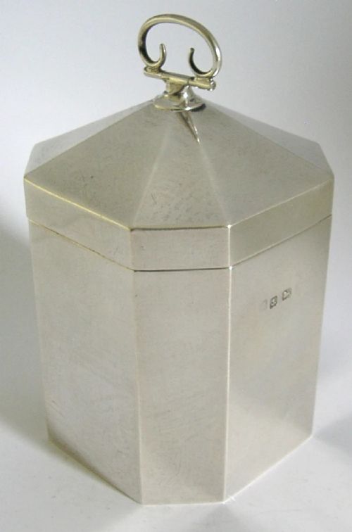 An octagonal sterling silver tea caddy featuring a faceted domed lid, scroll finial, and British hallmarks stamped near the rim. View III