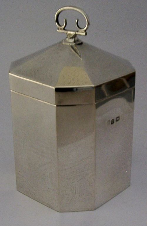 An octagonal sterling silver tea caddy featuring a faceted domed lid, scroll finial, and British hallmarks stamped near the rim. View V