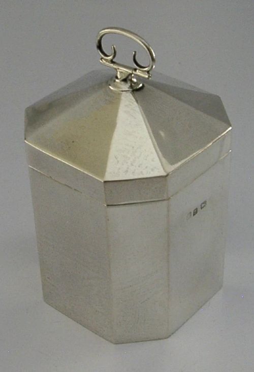 An octagonal sterling silver tea caddy featuring a faceted domed lid, scroll finial, and British hallmarks stamped near the rim. View VI