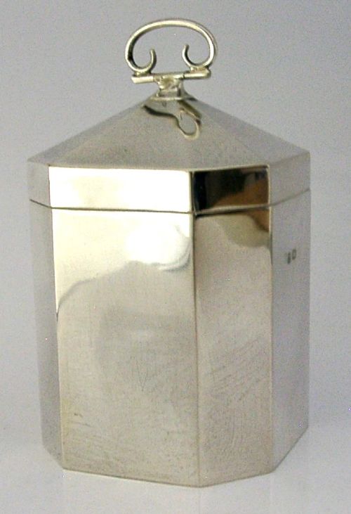 An octagonal sterling silver tea caddy featuring a faceted domed lid, scroll finial, and British hallmarks stamped near the rim. View VIII
