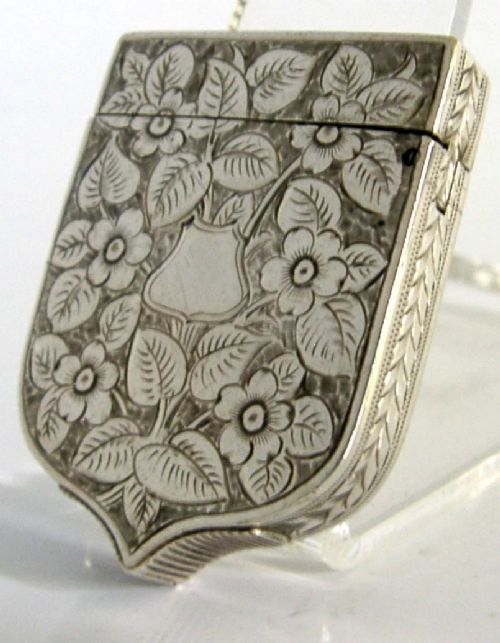 A Victorian shield-shaped sterling silver vesta case engraved with floral motifs and a central vacant cartouche.