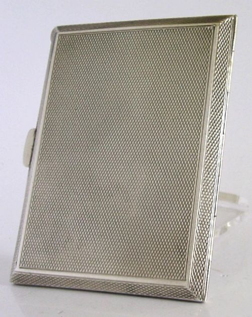 A square sterling silver hinged cigarette case showing an engine-turned textured exterior on one side and a white enamelled panel with hand-painted yellow and pink chrysanthemums on the other. View XI