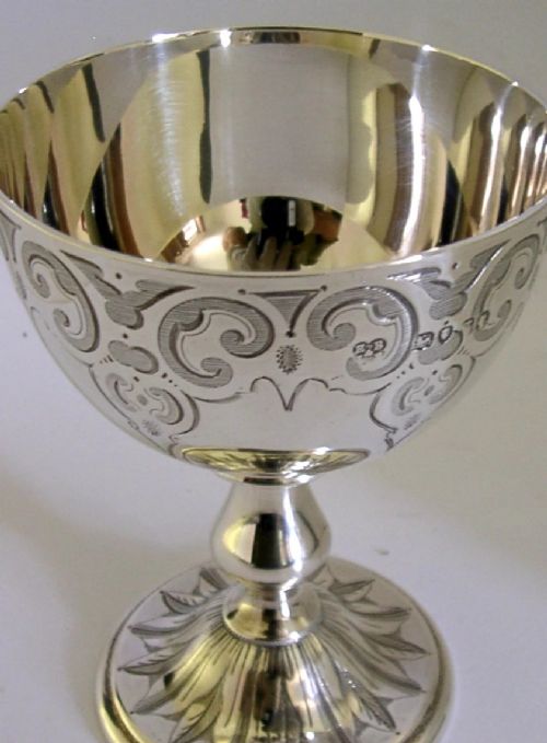 A mid-Victorian sterling silver chalice featuring an engraved scroll pattern around the cup, a central knopped stem, and a leaf-patterned circular base. View II