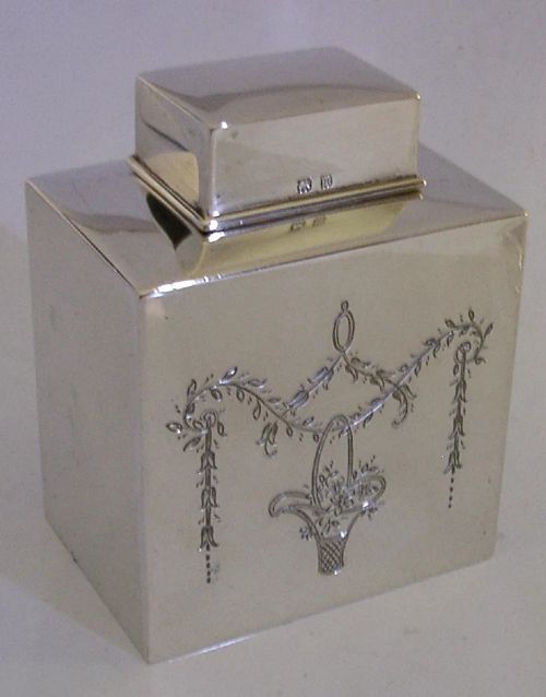 An antique Edwardian rectangular sterling silver tea caddy decorated with delicate engraved floral swags and a central flower basket, topped with a square cap lid. View V