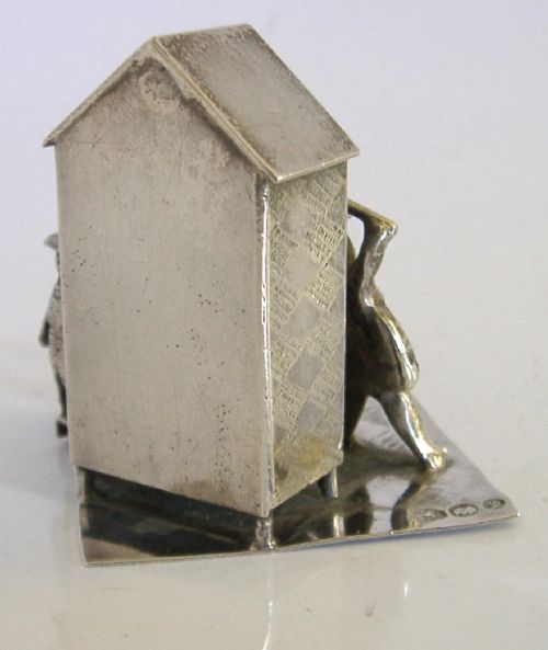 An 833 solid silver miniature model depicting a Punch and Judy puppet show booth with figures, an organ grinder, and a dog on a flat silver base. View V