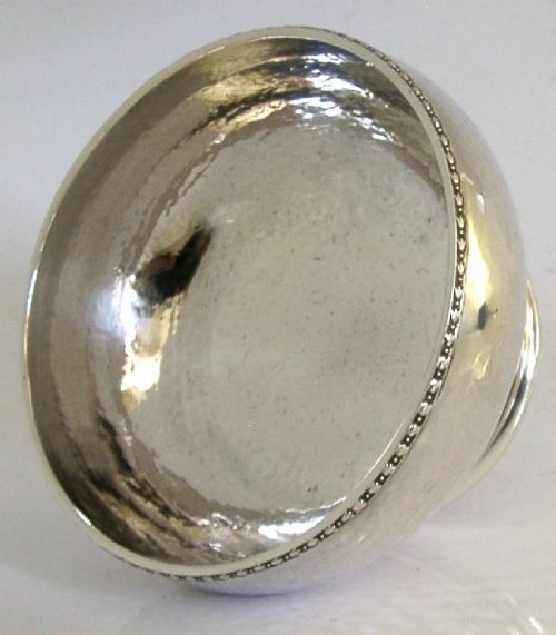 A planished sterling silver bowl featuring a hand-hammered finish, patterned rim, pedestal base, and British hallmarks stamped on the side. View V