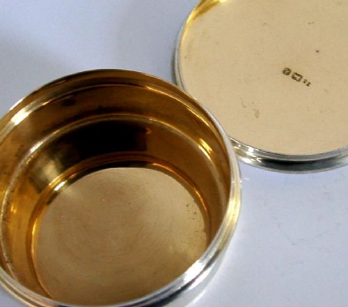 A small circular sterling silver pyx box featuring an engraved cross on the cover and a gold gilt interior. View V