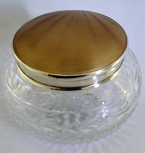 A circular cut glass vanity jar with a sterling silver rim and a bronze guilloche enamelled lid displaying a sunburst pattern. View IV