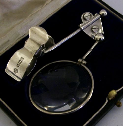 A sterling silver thumb magnifier glass with an adjustable arm clip rested inside a black velvet and silk lined presentation box. View II