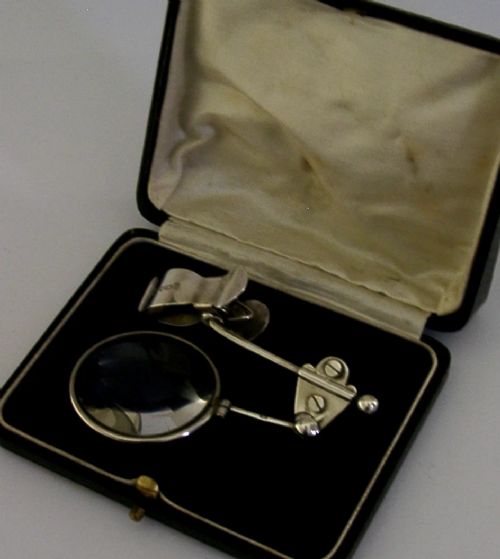 A sterling silver thumb magnifier glass with an adjustable arm clip rested inside a black velvet and silk lined presentation box. View VII