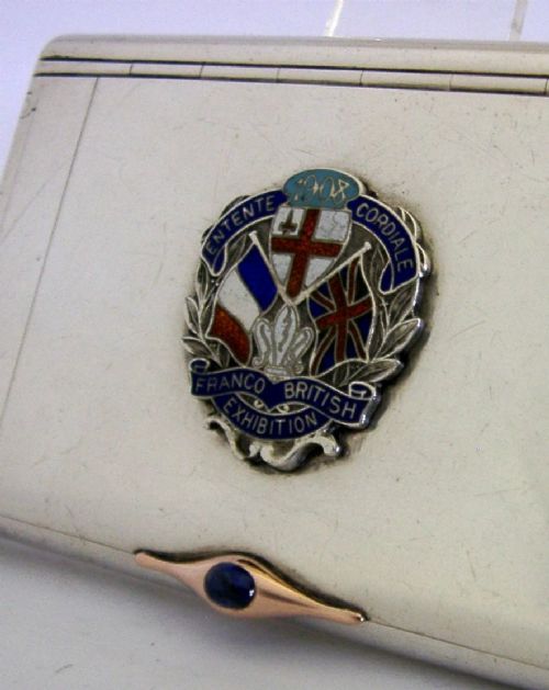 A rectangular silver cigarette case featuring a central enamel emblem depicting British and French flags with Entente Cordiale lettering and a gold thumbpiece. View VI