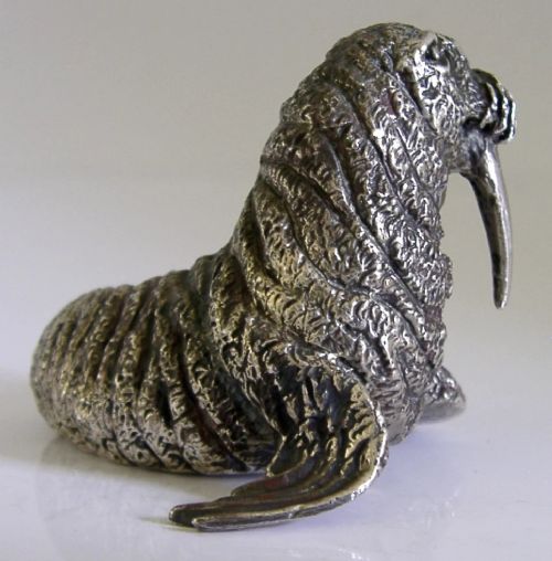 A detailed cast silver walrus figurine shown in profile with long downward tusks and textured skin. View VI