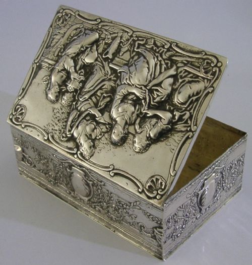 A rectangular silver box featuring embossed classical figures on the hinged lid and foliate scrollwork along the sides. View VI