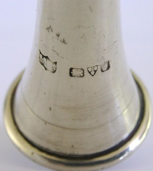 An Edwardian sterling silver hunting horn with ribbed body accents and a flared bell resting on a pale surface. View VI