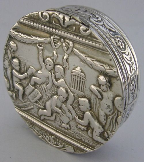 A circular antique silver trinket box featuring embossed relief depicting putti playing beneath floral garlands. View VIII