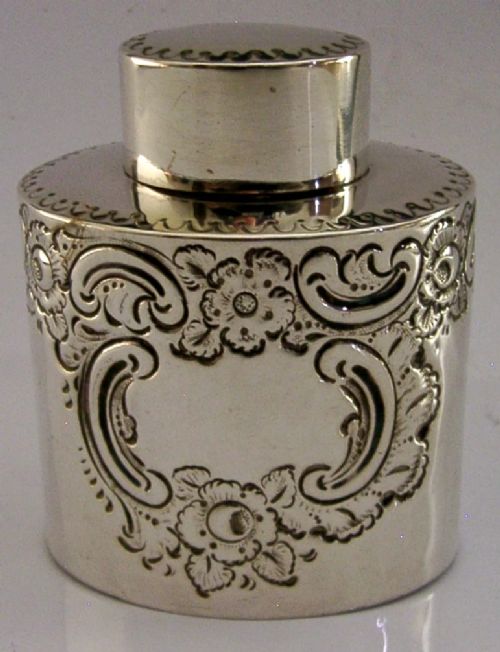 A cylindrical Victorian sterling silver tea caddy featuring chased floral and scroll motifs with a fitted cylindrical lid displaying hallmarks. View III