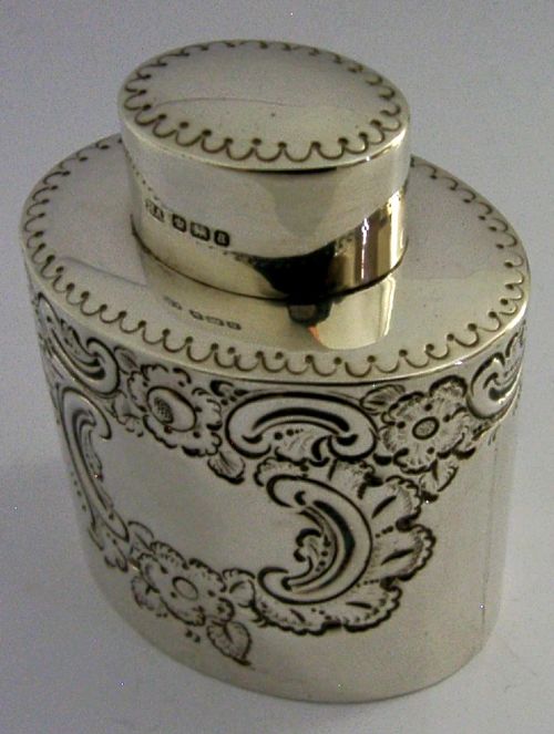 A cylindrical Victorian sterling silver tea caddy featuring chased floral and scroll motifs with a fitted cylindrical lid displaying hallmarks. View IV