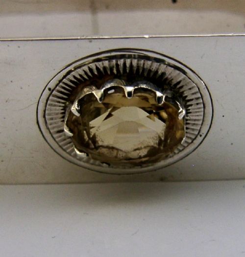 A polished rectangular sterling silver napkin ring set with a central oval citrine gemstone within a sunburst engraved surround. View V