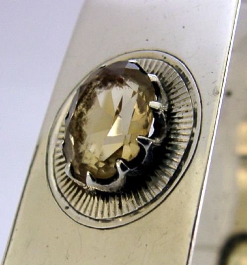 A polished rectangular sterling silver napkin ring set with a central oval citrine gemstone within a sunburst engraved surround. View VII