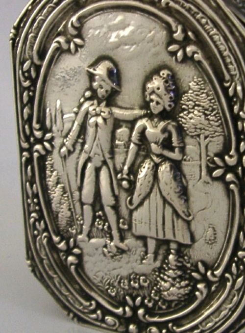 An octagonal antique silver table box featuring a detailed repousse scene of a couple in 18th-century attire within a scrollwork frame. View V