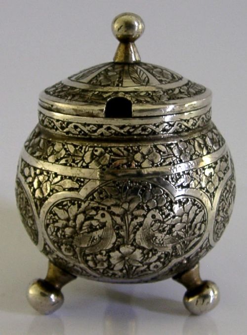 An antique hand-engraved solid silver mustard pot featuring arabesque foliage patterns, a hinged lid with finial, a spoon aperture, and three ball feet. View II